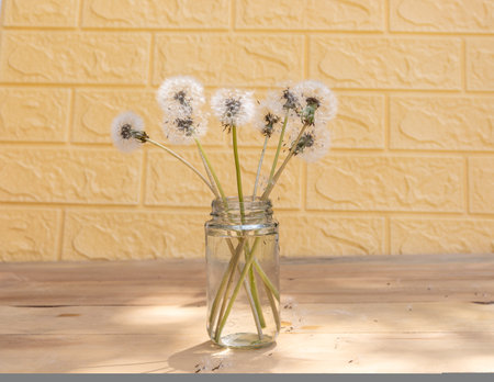 A bouquet of dandelions in a transparent glass jar on a wooden table with bricks backgroundの写真素材