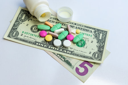 Medicine pills and tablets scattered from a bottle on US dollar bills. Health care expenses concept.の写真素材