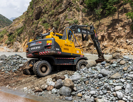 Excavator working to strengthen the protection wall at the river bank to prevent the river water entering the Bahrain bazar:Bahrain swat, Pakistan - June 12, 2023.のeditorial素材