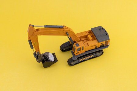 Excavator with ethereum coin on yellow background. Toy excavator carrying crypto coin in its bucket. Crypto currency mining concept.の写真素材