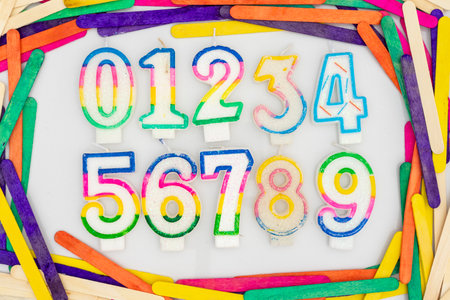 Multicolored numerical numbers set from zero to nine 0123456789 shape candles in a colorful sticks frame border on white backgroundの写真素材
