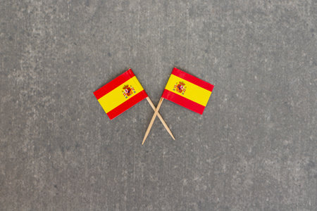 Two Crossed Mini Spanish Flags on Toothpicks Over Gray Backgroundの写真素材