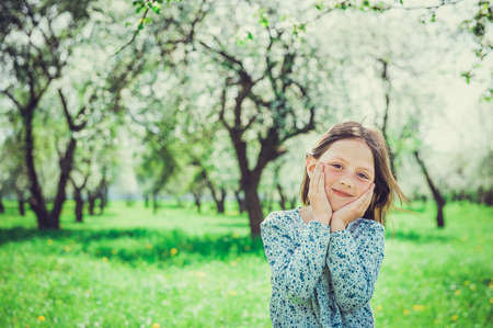Smiling little girl in the garden, holding hands your face. Child in spring fruit orchard.の写真素材