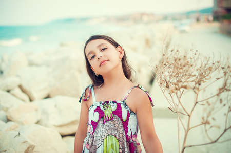 Beautiful little girl in dress on the sea, standing with dry flowerの写真素材
