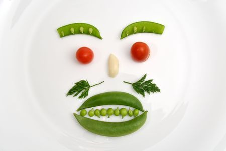 Vegetable face made of peas, parsley, tomato and garlic on a white plateの写真素材