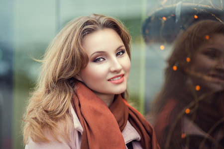 Smiling beautiful young business woman in warm clothing enjoying time outdoors in winter holiday time. beauty outdoor double  portrait reflection near a shop store window with Christmas lights on itの写真素材