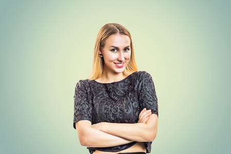 Content blond woman wearing stylish blouse and standing with hands crossed looking at cameraの写真素材