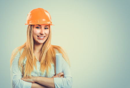 Professional content woman in white shirt wearing orange hardhat and holding paper rollの写真素材