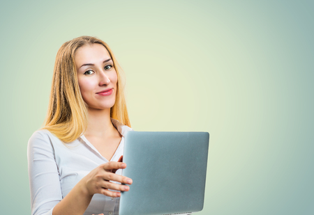 Smiling confident blond woman holding laptop and looking at camera on gray backgroundの写真素材