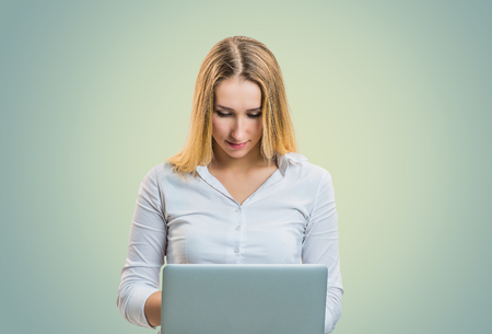 Casual modern blond woman in white shirt using laptop on gray backgroundの写真素材