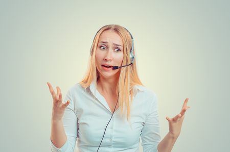 Young blond woman in white shirt wearing headset in puzzlement and gesturing in helplessnessの写真素材