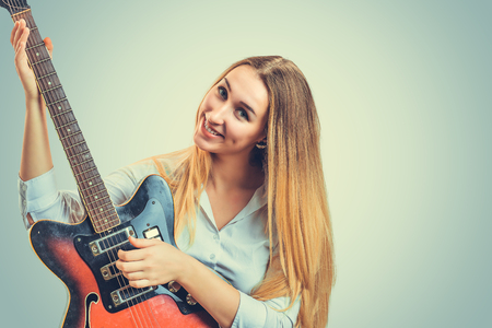 Coquette young blond woman playing electric guitar and smiling at camera on gray backgroundの写真素材