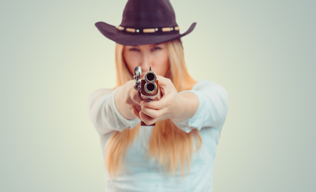 Blurred woman in cowboy hat aiming at camera with double-barreled gun on gray background
