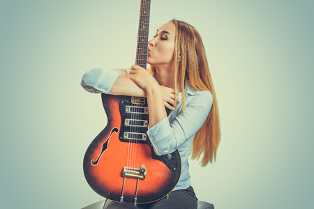 Young devoted woman sitting on gray background and kissing electric guitarの写真素材