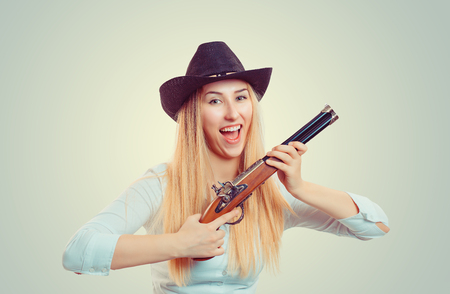 Venturous blond woman wearing cowboy hat and holding double-barreled gun looking at cameraの写真素材