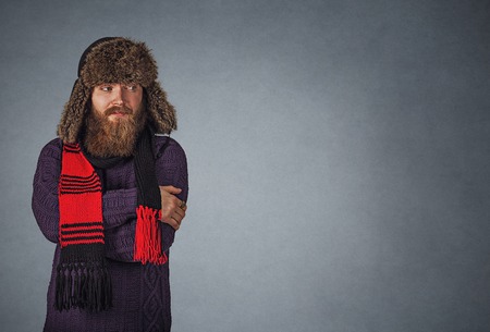 I am cold. Bearded man in fluffy russian fur hat, Young male making cold gesture looking to the side to copy space Isolated on gray grey studio wall Background. Neutral face expression, human emotion.の写真素材
