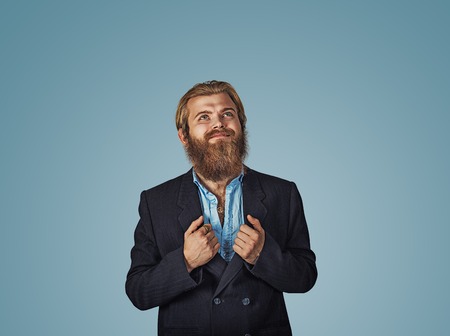 Bearded hipster business man hands on suit showing super hero shirt rising his head looking up and smiling Isolated on blue Background. Negative face expression, human emotion, body language, reactionの写真素材
