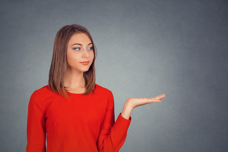 Closeup portrait happy confident young smiling woman gesturing presenting copy space at right with palm up isolated gray grey wall background. Positive human emotion sign symbol face expression feelingの写真素材
