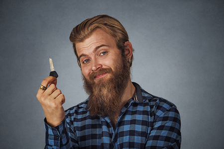 Bearded business man, young handsome man holding car key or new apartment Isolated on gray grey studio wall Background. Positive face expression, human emotion, body language, reaction, attitudeの写真素材