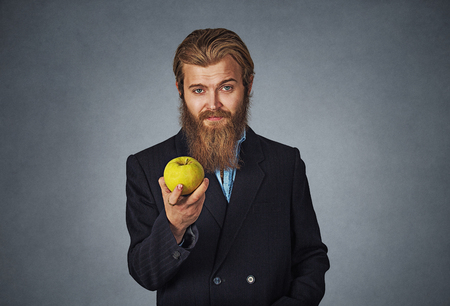 Diet concept. Businessman Bearded hipster business man showing giving holding a green apple in his hand Isolated on gray grey studio wall Background. Positive face expression, emotion, body language.の写真素材