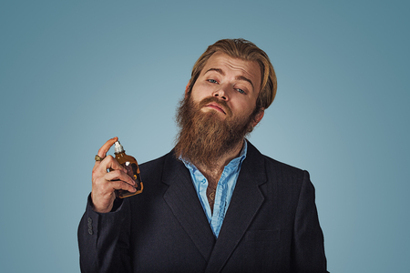Rich hipster bearded man using expensive perfume eau de cologne perfume isolated on blue background. Positive face expression, human emotion, body language, reaction, attitude. Studio Horizontal shot.の写真素材