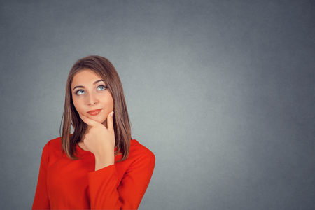 Thoughtful woman in red dress. Portrait happy beautiful woman thinking looking up isolated grey wall background with copy space. Human face expressions, emotions, feelings, body language, perceptionの写真素材