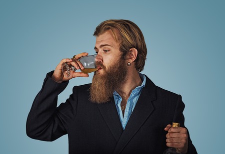 Handsome bearded well-dressed man in jacket holding tasting drinking glass of beverage whiskey alcohol isolated on grey gray studio background wall. drinks, relax, leisure and people concept.の写真素材