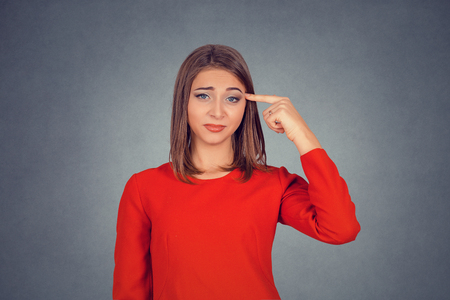 Angry mad woman gesturing with finger against temple are you crazy. Business woman in red dress, bob hairstyle. Isolated on gray grey studio wall Background. Negative face expression, human emotion.の写真素材