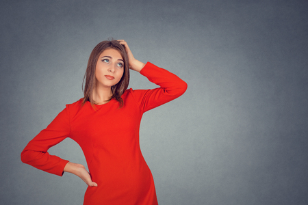 Thinking. Closeup portrait young woman scratching head, pondering daydreaming deeply about something looking up isolated on gray wall background. Human facial expression emotion feelings sign symbolの写真素材