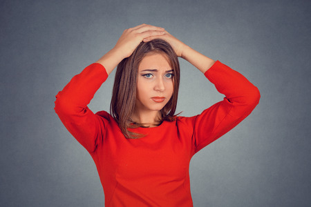 Portrait stressed out young woman with worried face expression hands on her head looking at you camera. Business lady in red dress bob hairstyle. Isolated on gray grey studio wall Background. Negativeの写真素材