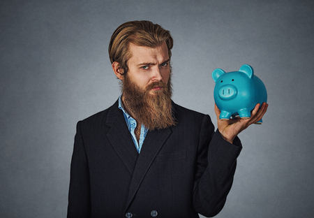 Finance, money. Serious man holds piggy bank. Bearded man holds piggy bank full of money over gray background. Business and financial; finance measurement concept. Business man save money in piggybankの写真素材