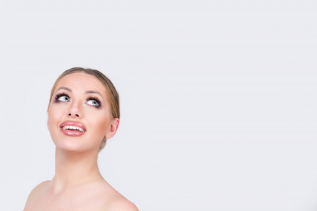 Adult positive pretty elegant woman standing on gray background while thinking, dreaming and looking away up to the side in studio light gray white background.の写真素材