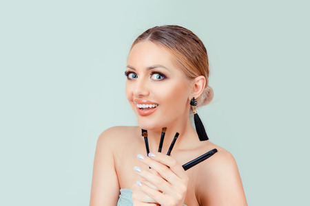 Super excited beauty makeup artist. Closeup blonde hair beautiful young woman pretty smiling funny fashion girl holding eyeshadow brushes looking at you camera isolated on light green wall backgroundの写真素材