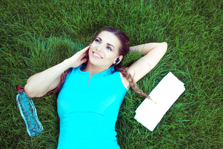 From above shot of young fit sportswoman lying on green grass and listening to music with headphonesの写真素材