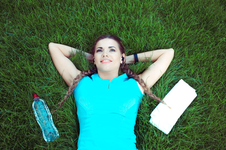 From above of young fit sportswoman lying on green lawn with bottle of water and towel in relaxationの写真素材