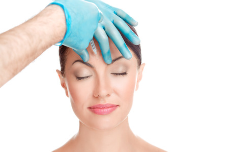 Woman having injected filler botulinum toxin injection hyaluronic acid shot anti wrinkles aesthetic surgery in forehead done by doctor in cosmetic clinic, eyes closed relaxed isolated white backgroundの写真素材