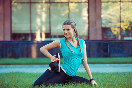 Happy slim sportswoman training on meadow and stretching legs smiling away