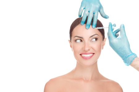Happy woman receiving hyaluronic acid botulinum toxin injection in her forehead in medical office, looking to the side needle happy smiling, isolated on white background with copy space Beautify conceptの写真素材