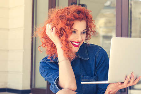 Pretty female student with cute smile looking at net-book laptop while relaxing after lectures near University on stair, beautiful happy woman working on laptop computer during coffee break outdoorsの写真素材