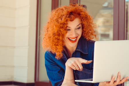 Attractive young woman looking at laptop and pointing with finger at her pad computer standing outdoor in park on sunny summer dayの写真素材