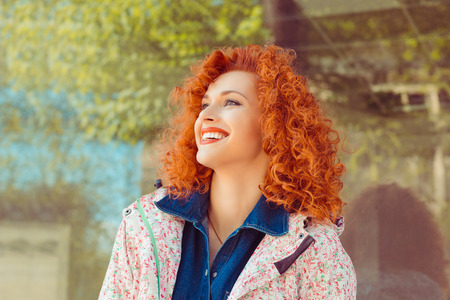 Outdoors portrait of beautiful young redhead curly girl laughing in a bus station. Positive human emotions, face expression, reaction, feelings.の写真素材