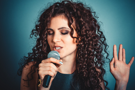 Singer. Closeup portrait head shot sexy beautiful happy young woman lady girl singing with eyes closed at karaoke with microphone isolated blue background wall. Positive human emotion expressionの写真素材