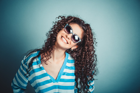 Headshot of a happy smiling woman in sunglasses isolated on blue wall background laughing. Positive face expression, human emotion, body language, reaction.の写真素材