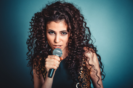 Woman unhappy talking by microphone looking skeptical to you camera isolated blue background. Negative face expression, human emotion, reaction, attitudeの写真素材