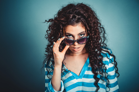 Surprised shocked frustrated young woman holding sunglasses down looking above them skeptically isolated blue wall background. Negative face expression, human emotion, reaction, body languageの写真素材