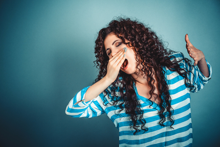 It is too early for me. Closeup portrait sleepy young woman with wide open mouth yawning eyes closed looking bored isolated blue wall background. Face expression emotion body languageの写真素材