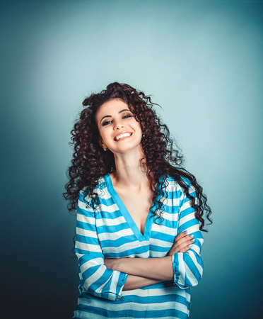 Success. Closeup portrait head shot confident beautiful happy young brunette curly woman arms crossed smiling isolated blue background wall. Positive emotion face expression feeling life perceptionの写真素材
