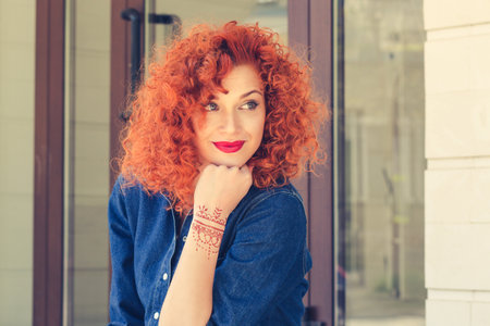 Pensive about new job new life. Beautiful red head curly woman person girl looking to side thinking about future boyfriend family deciding what to do isolated outdoor street apartment complex backgroundの写真素材