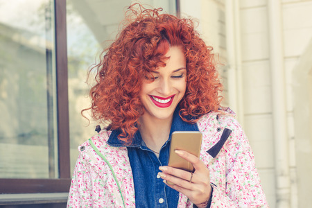 Girl walking smiling and texting on the smart phone in the street wearing a white floral jacket in spring.の写真素材