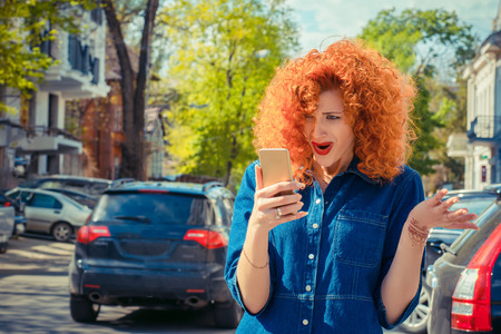 Shocking SMS. Closeup portrait funny shocked anxious scared young girl talking at phone receiving bad news photos message with disgusting emotion on face on cityscape background. Human reactionの写真素材